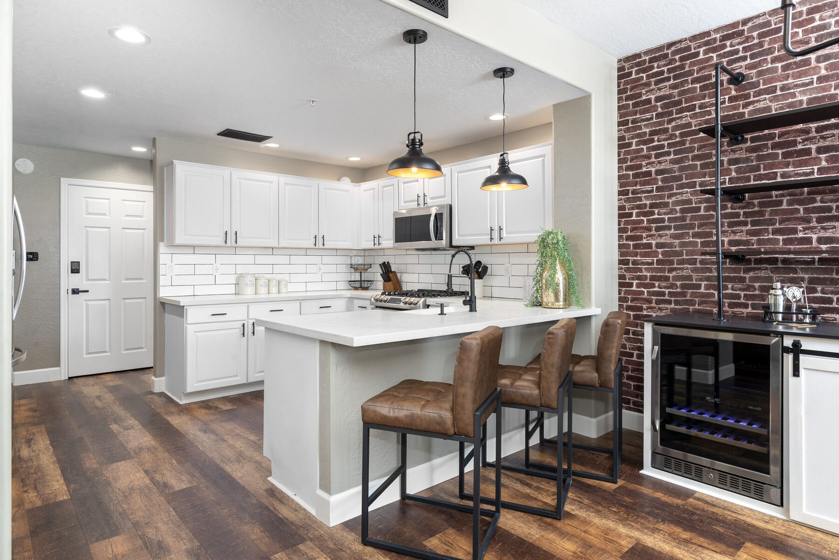 Kitchen with white cabinetry, island bar seating, brick wall, and dual-zone wine fridge